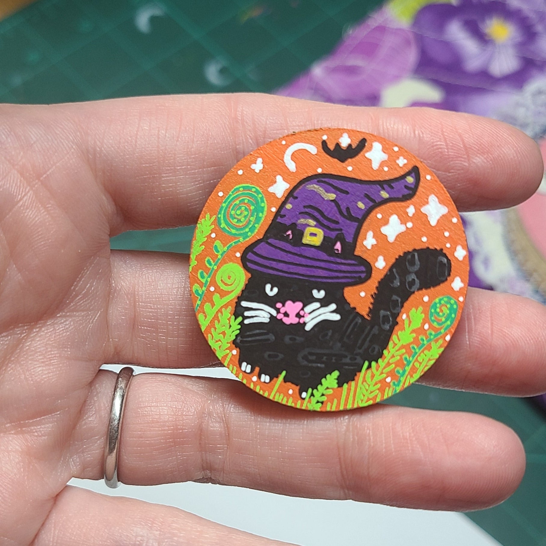Hand holding a colorful Halloween-themed needle minder with a black cat and witch hat design.