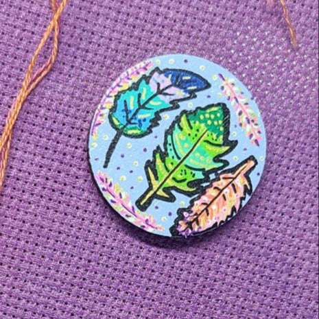 Colorful painted leaf design on small needle minder on fabric