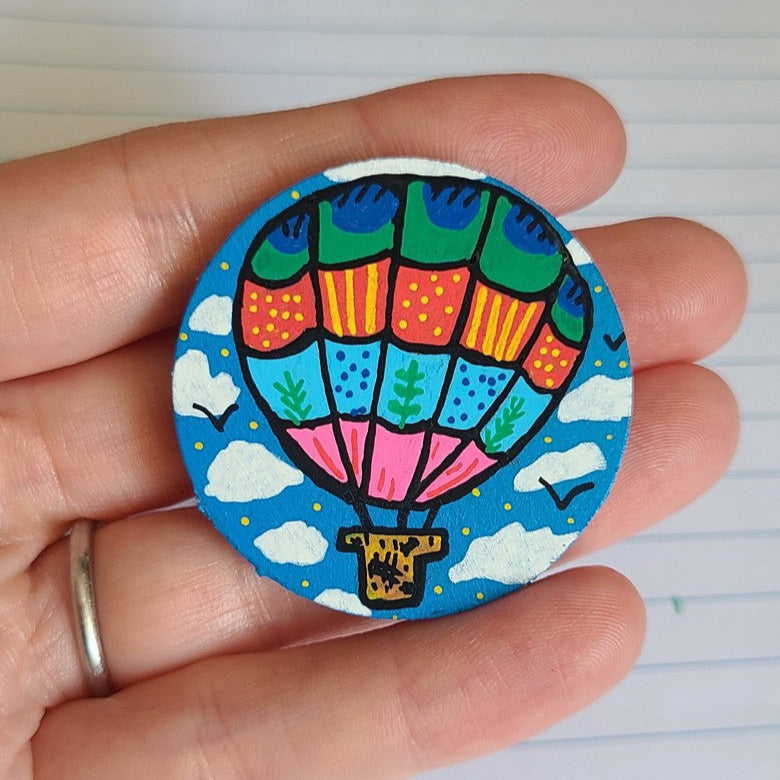 Colorful hot air balloon button held in a hand against a lined paper background
