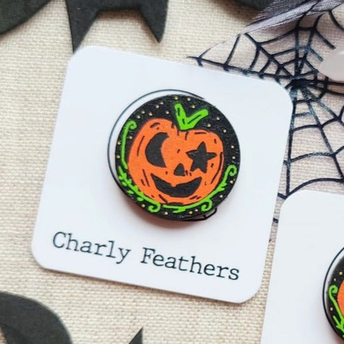 Two Halloween-themed needle minders on cards with 'Charly Feathers' branding, surrounded by spider webs and a purple potion bottle.