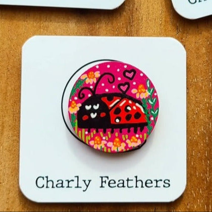 Three colorful needle minders with ladybug designs on cards labeled 'Charly Feathers' on a wooden surface.
