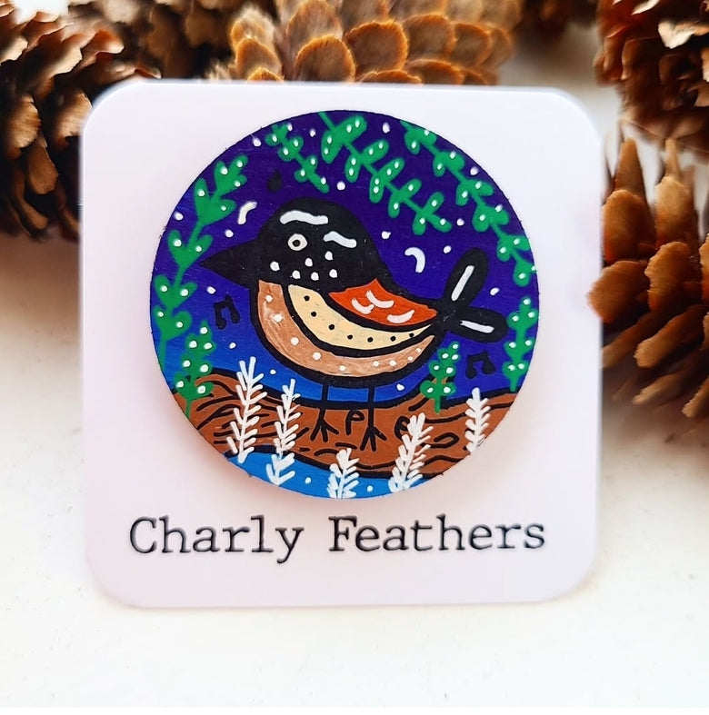needle minder with a nuthatch bird illustration and 'Charly Feathers' branding, surrounded by pine cones.