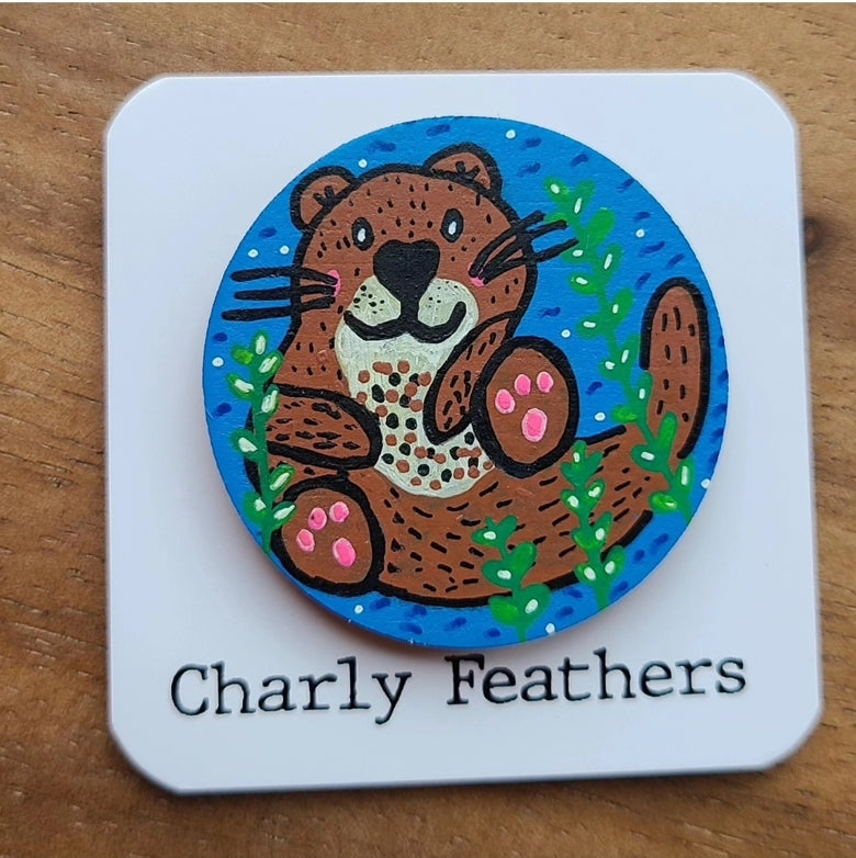 minder with a cartoon otter design and 'Charly Feathers' branding on a wooden surface.