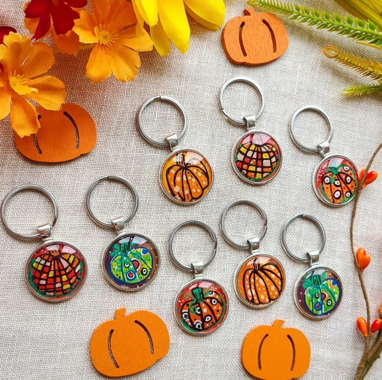 Colorful keychains with pumpkin designs on a textured surface with flowers and leaves.