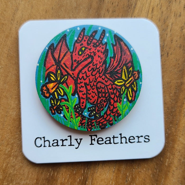 Colorful dragon design on a badge with 'Charly Feathers' branding, placed on a wooden surface.