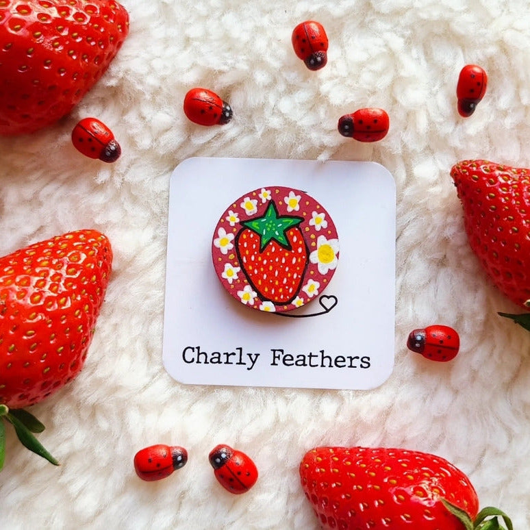 Strawberry-themed needle minder with 'Charly Feathers' branding surrounded by strawberries and ladybugs on a fluffy white surface.