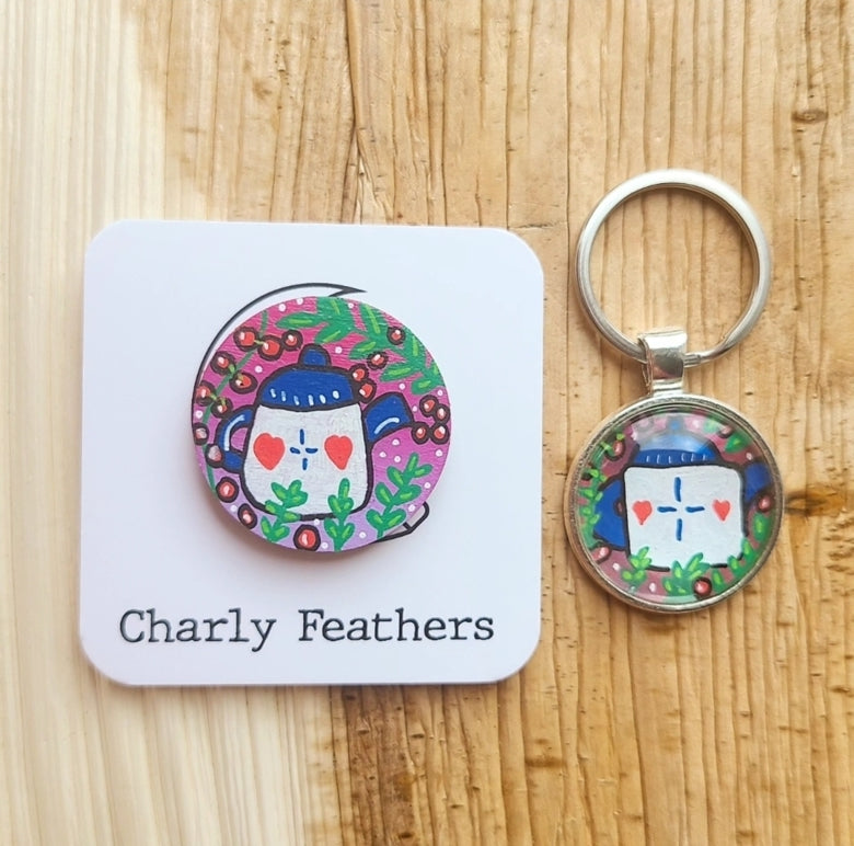 Keychain and needle minder with colorful teapot design on a wooden surface, featuring 'Charly Feathers' branding.