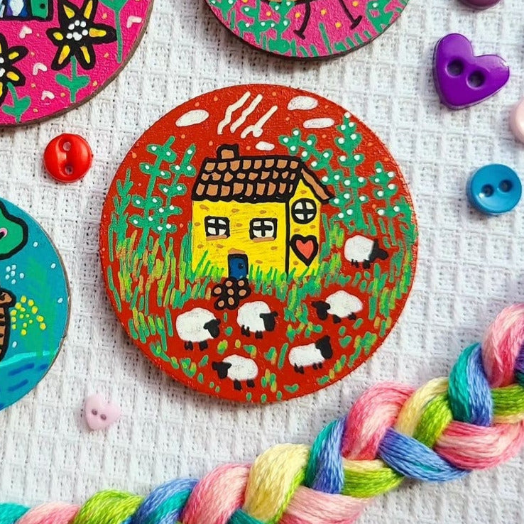 illustration of yellow house and sheep on a large needle minder